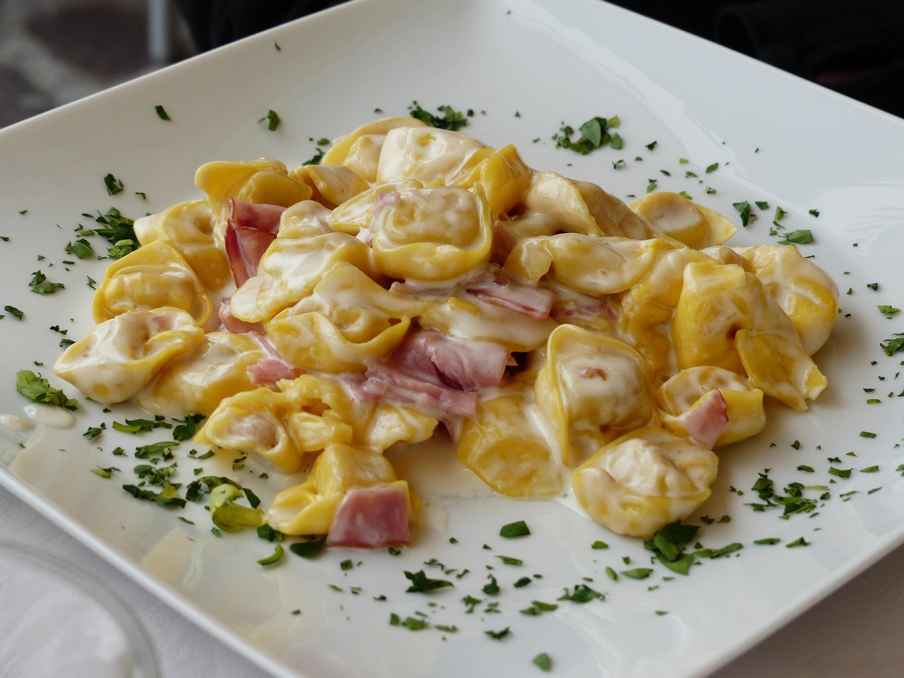 Tortellini fumanti serviti su un piatto, con un castello medievale sullo sfondo in Emilia-Romagna.